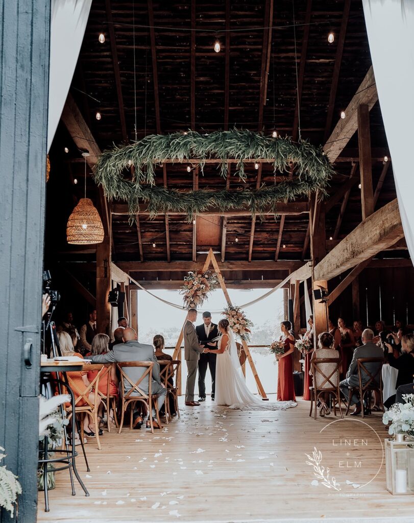 Barn wedding ceremony wide shot with greenery chandelier and fall colors