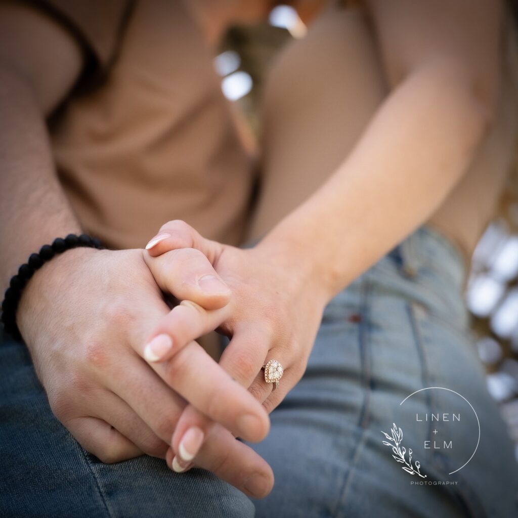 Engagement ring in foreground shot from ground with couple kissing in background