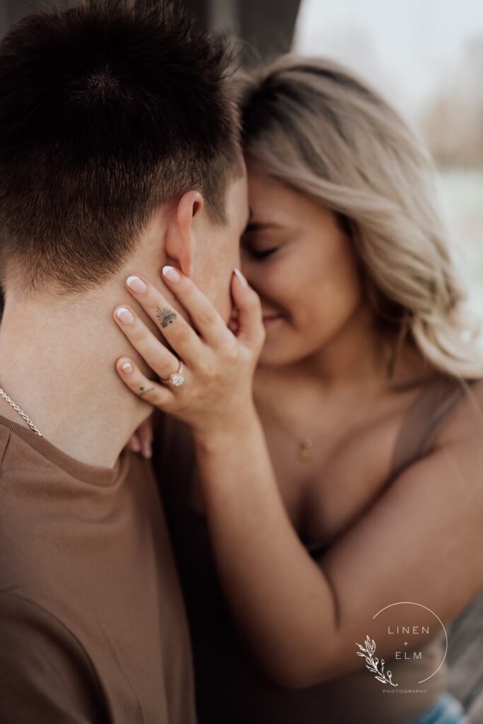 Over the shoulder moody shot of couple embracing featuring engagement ring